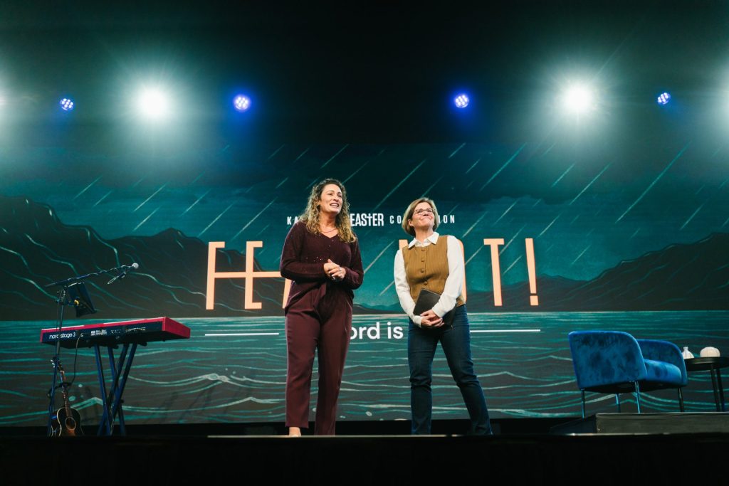 Two women speaking on stage at Katoomba Easter Convention with lighting and backdrop.